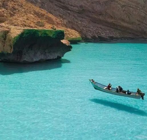 Дерев'яний човен з людьми на прозорій бірюзовій воді біля скелястого берега Сокотри